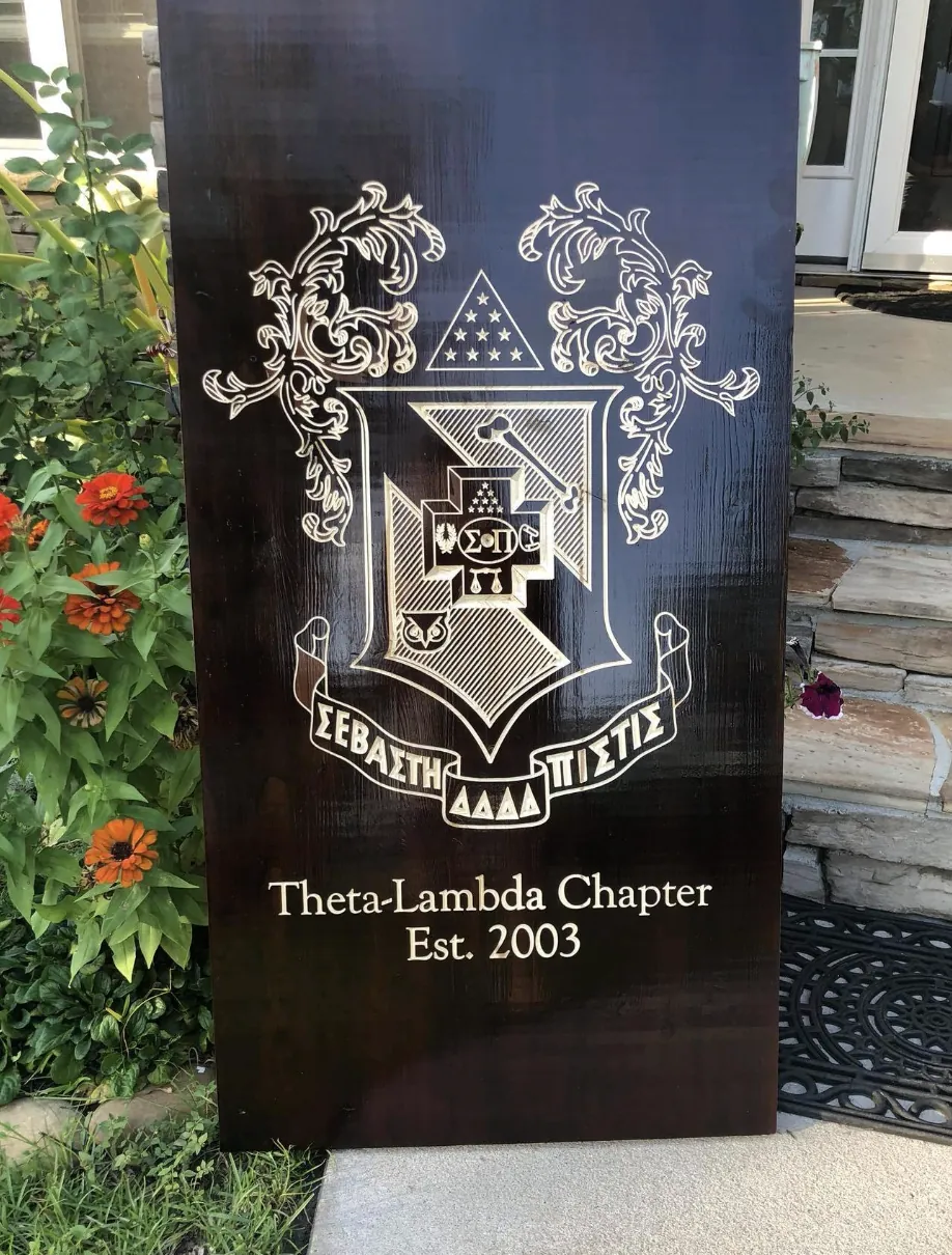 Theta-Lambda Chapter crest engraved on a dark wood panel