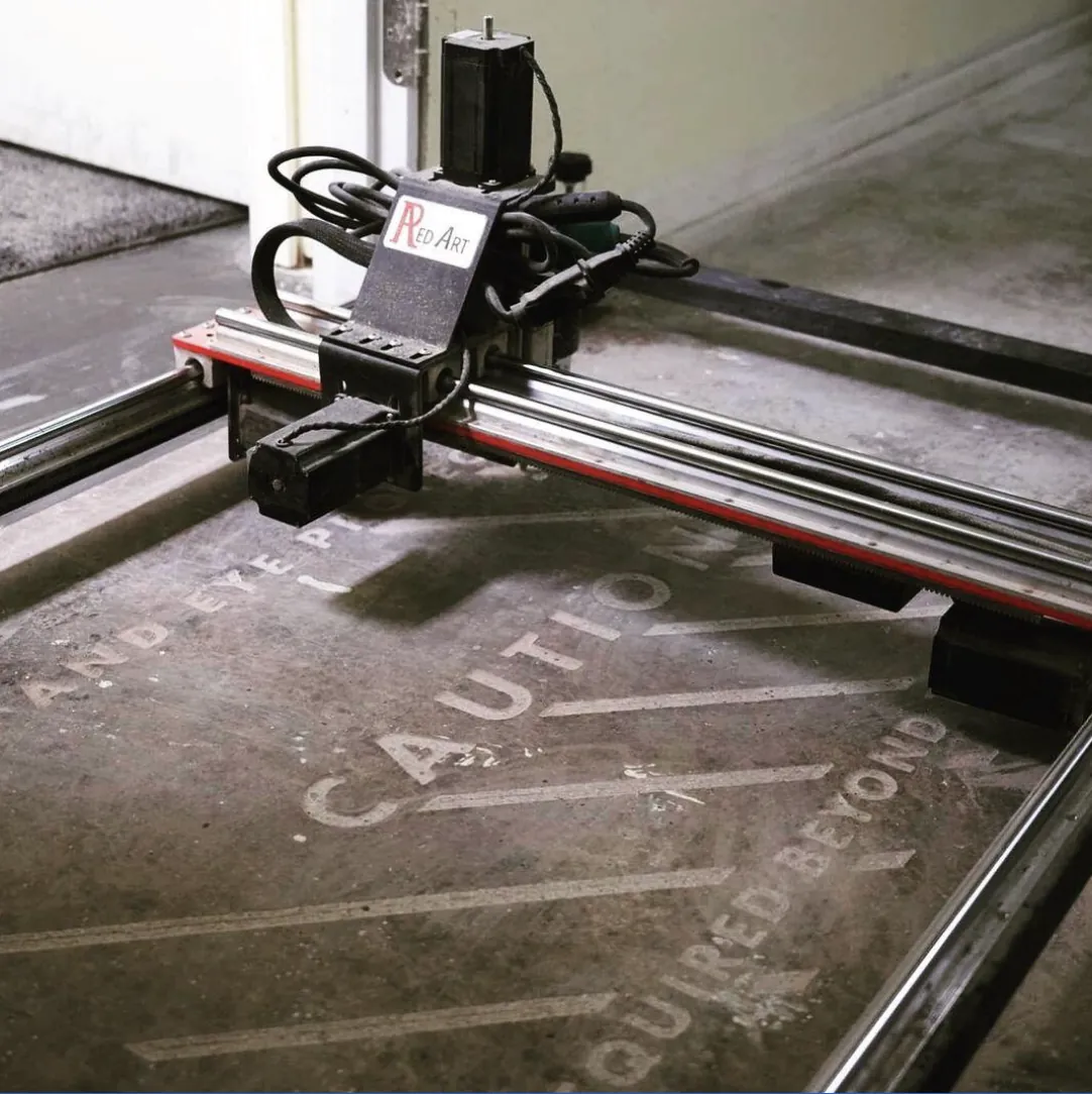 Red Art engraving machine cutting caution lettering into concrete